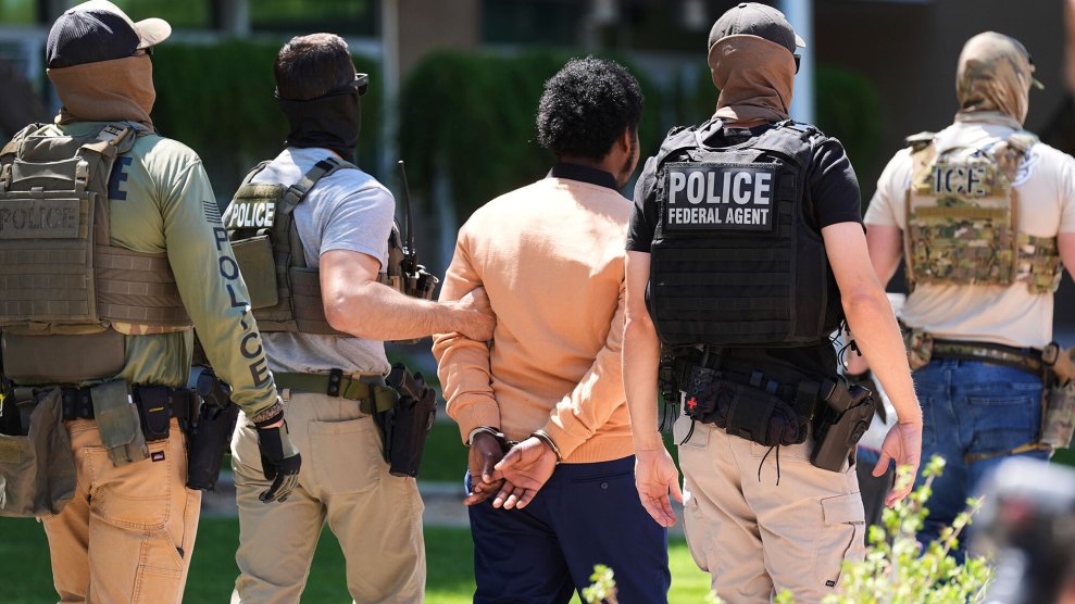Four law enforcement officers walk with a man in handcuffs, their backs toward the camera.
